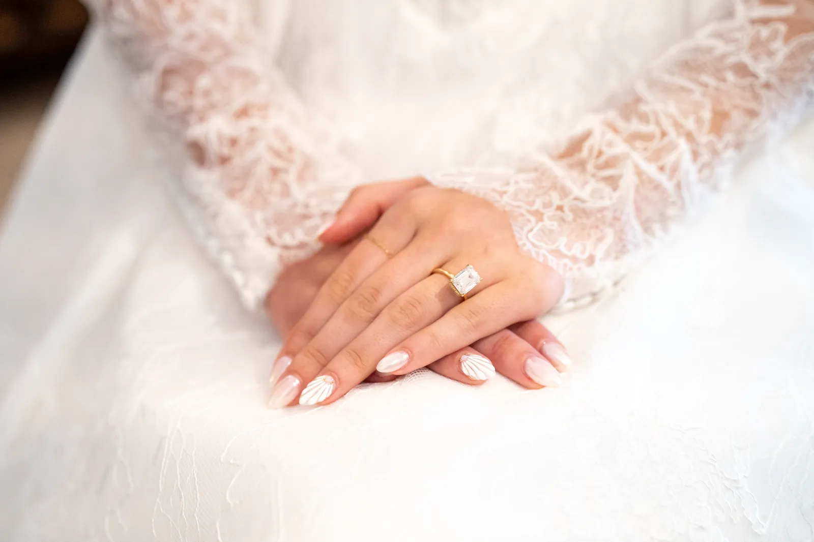 Manos de la novia con el anillo de compromiso sobre el encaje del vestido