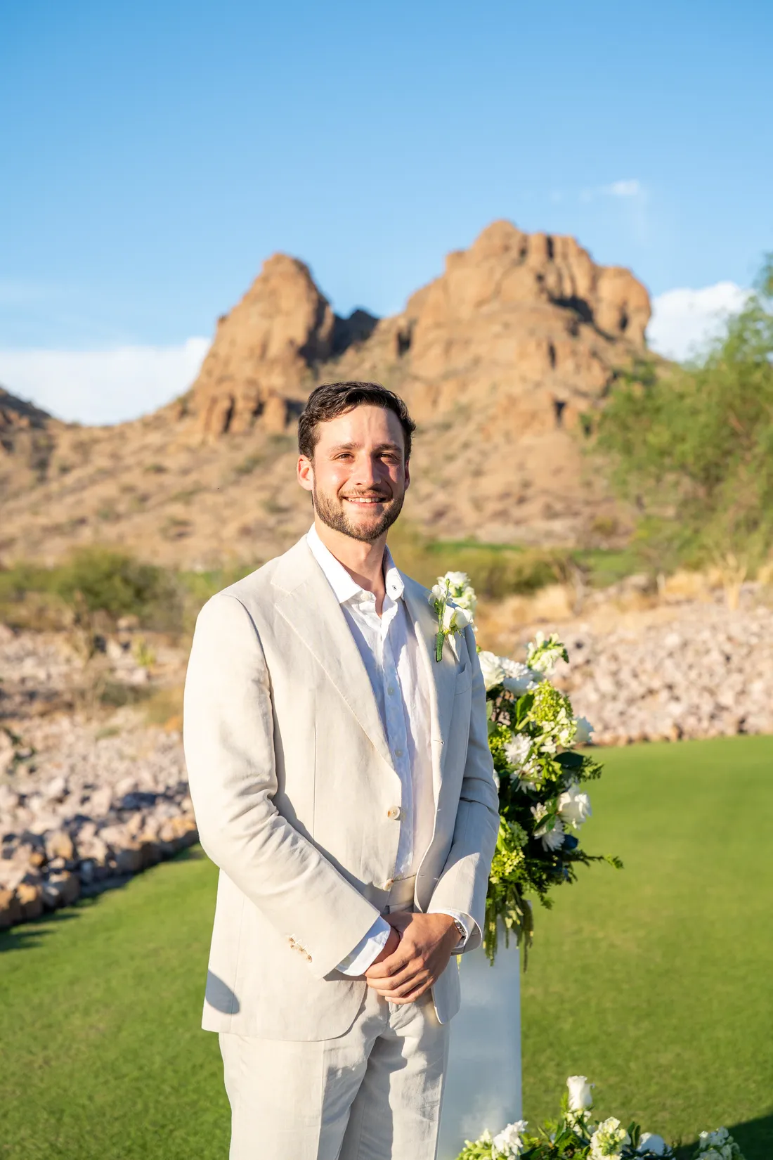 El novio espera junto al arreglo floral, con los cerros del desierto atrás