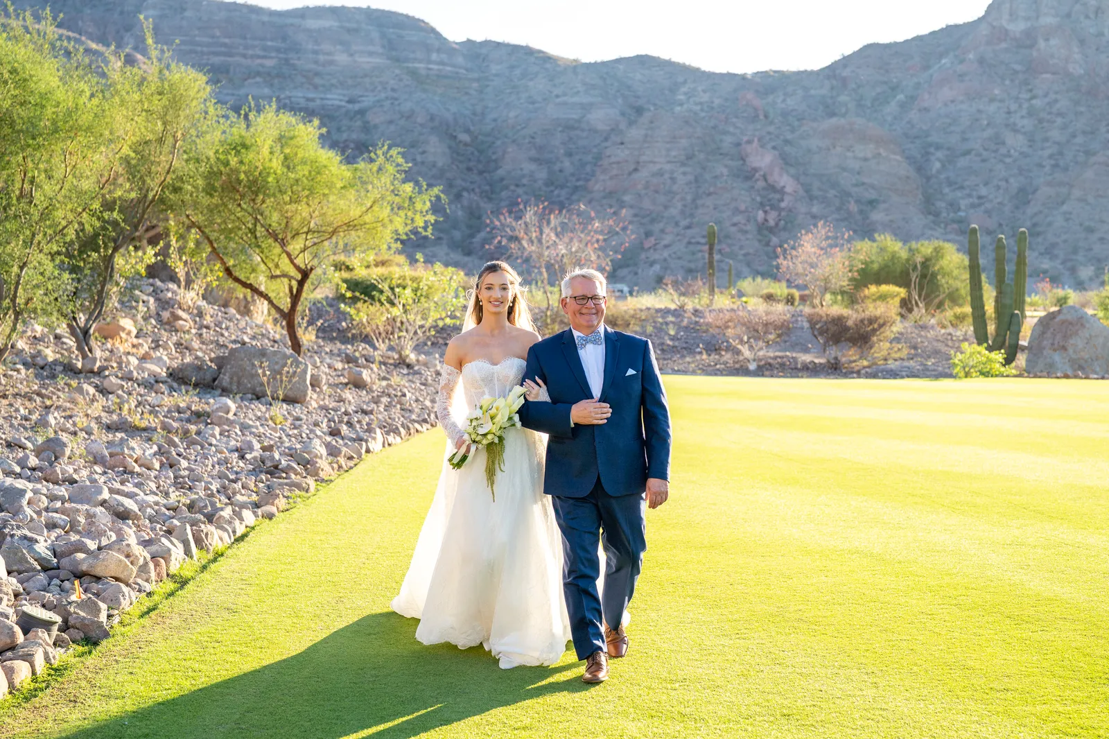 La novia entra del brazo de su papá por el pasto del campo de golf