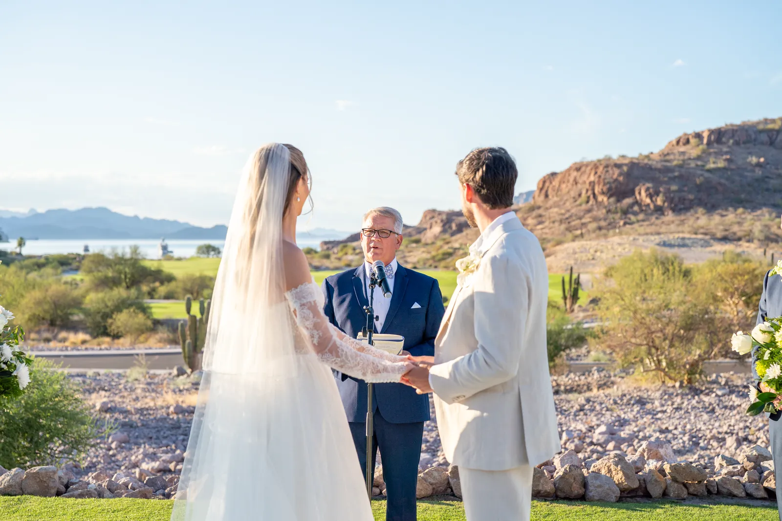 Los novios se toman de las manos durante la ceremonia, con el mar detrás