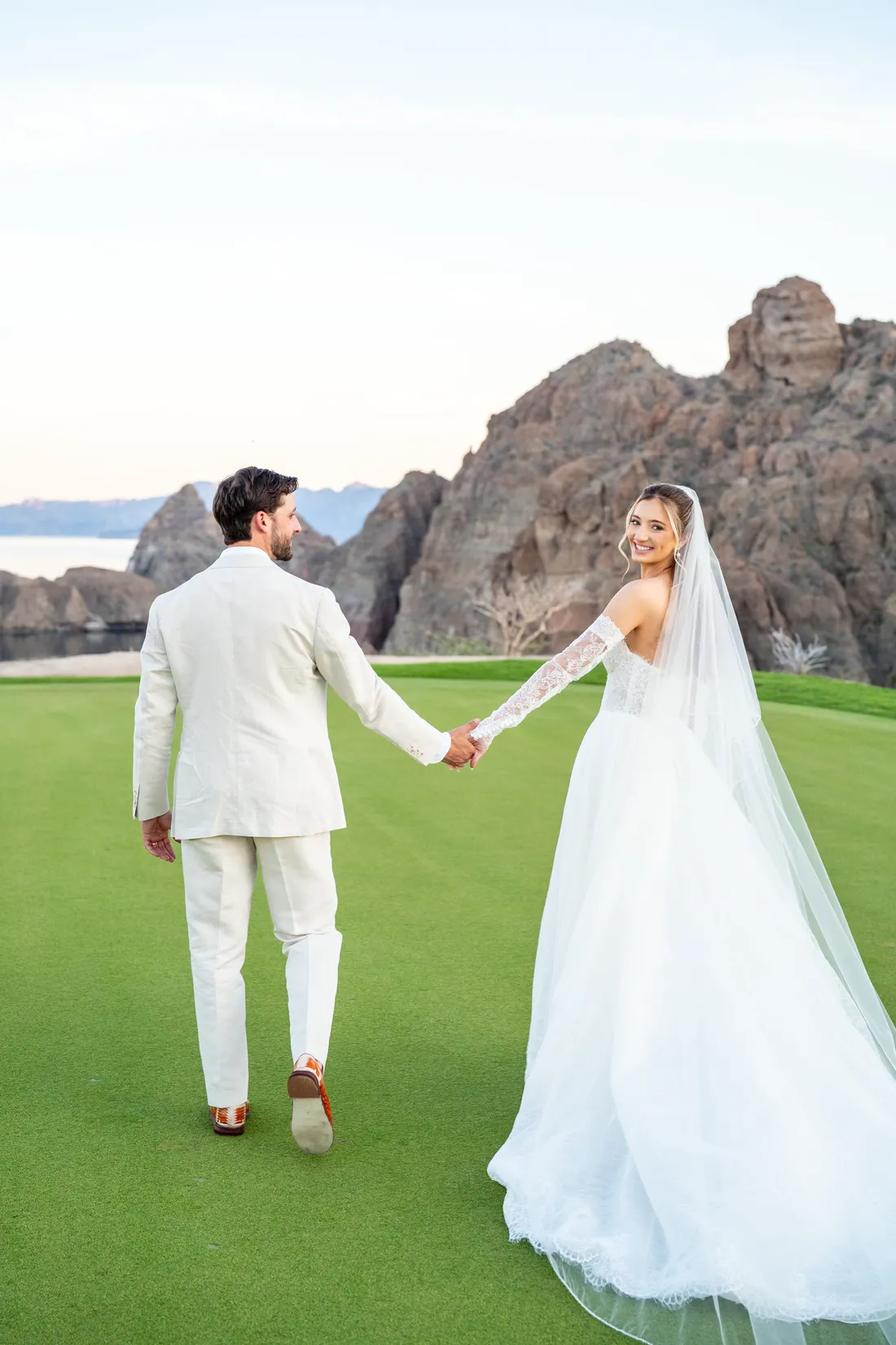 Los novios caminan de la mano hacia los acantilados del campo de golf