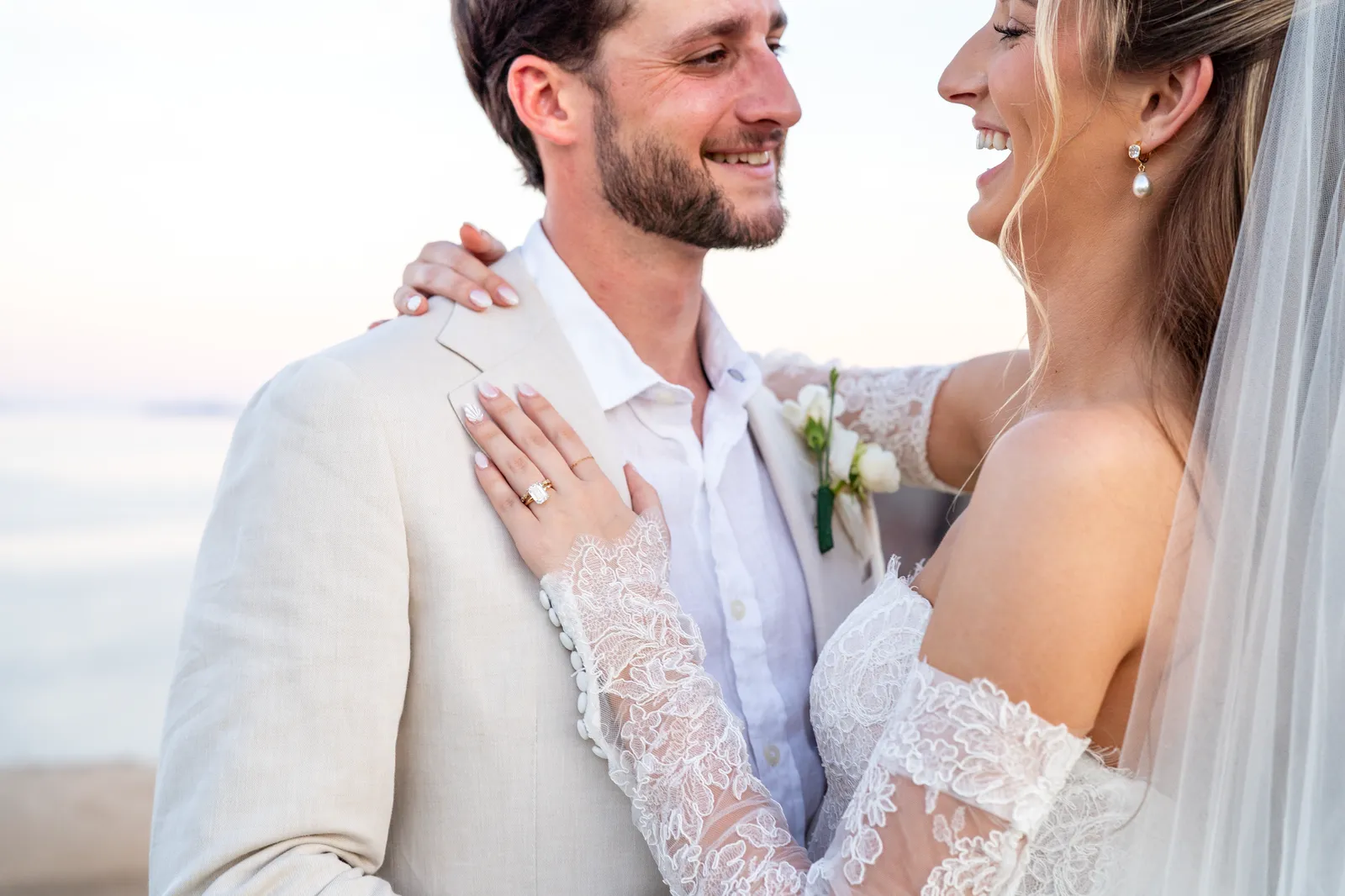 Los novios abrazados riendo, con el mar al fondo