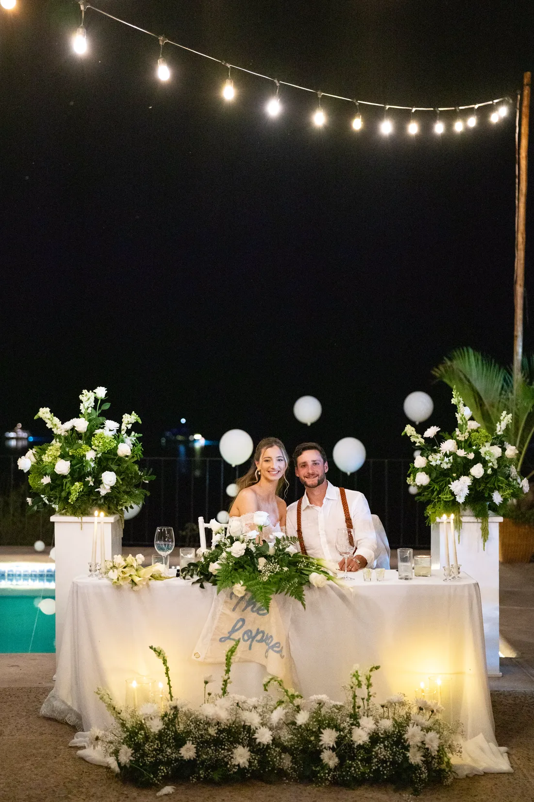 La mesa de los novios iluminada junto a la alberca, bajo las series de luces