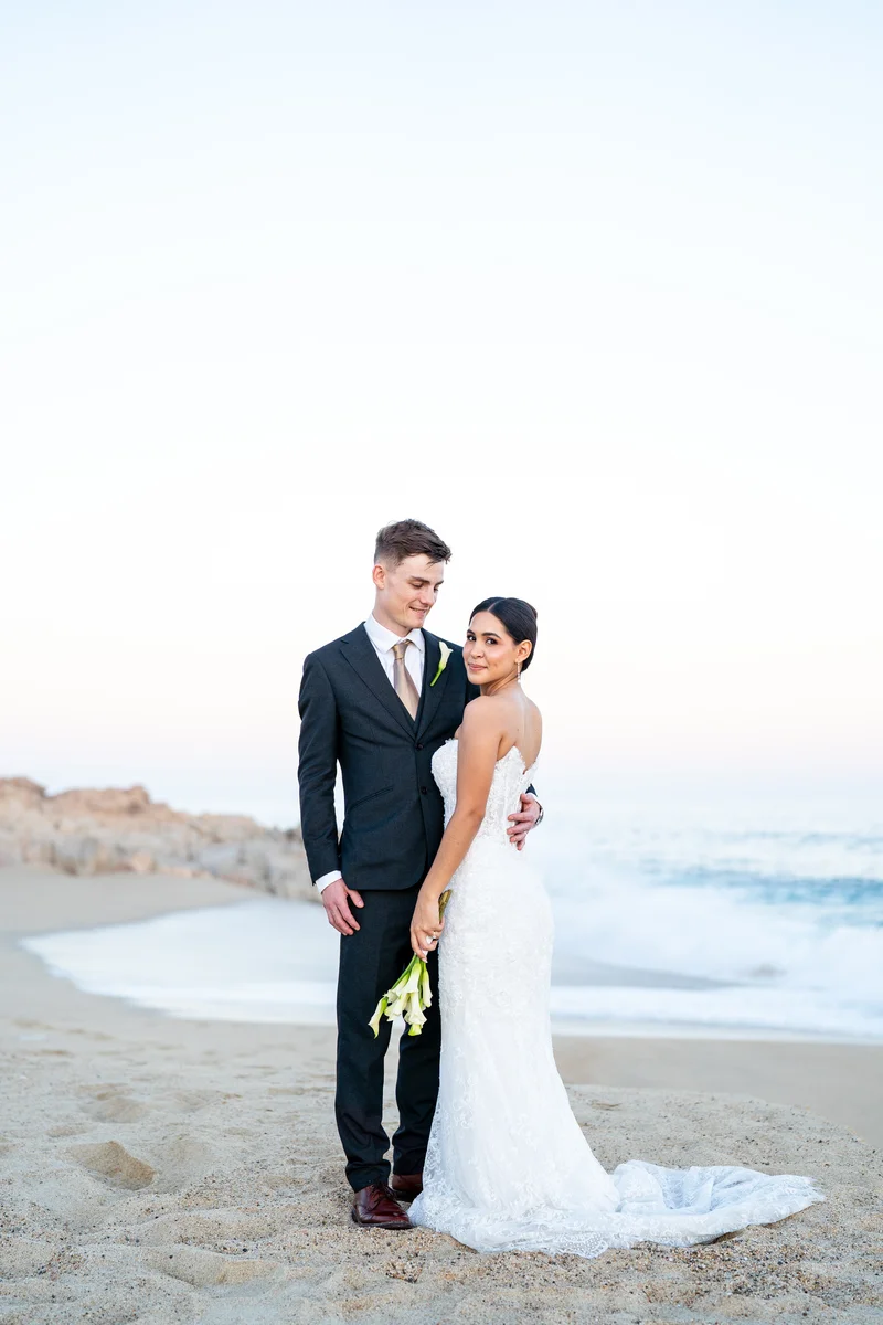 Los novios posan en la playa al anochecer con el ramo de alcatraces