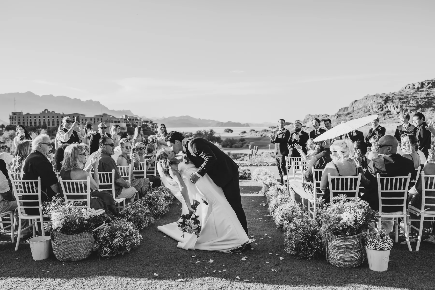 Los novios se besan al final del pasillo mientras sus invitados aplauden en una ceremonia al aire libre