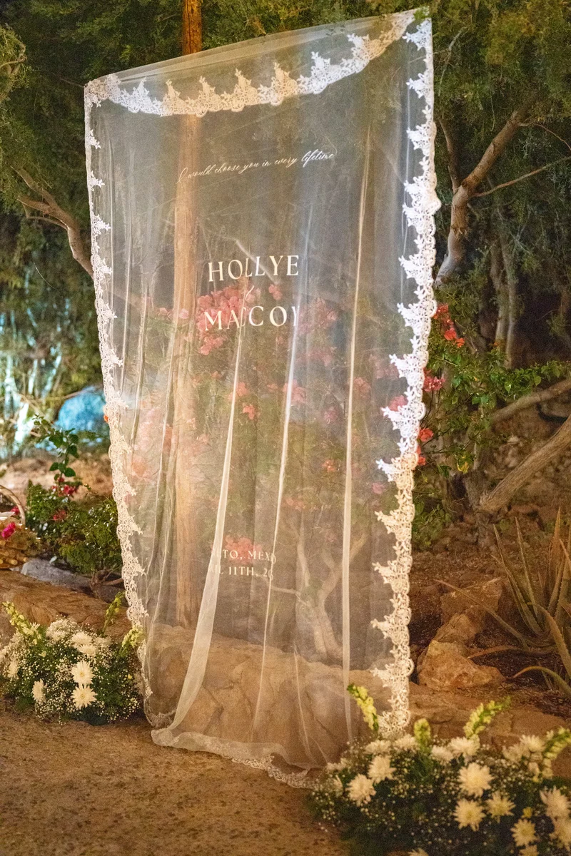 Letrero de bienvenida de la boda sobre velo de encaje, iluminado entre la vegetación del jardín