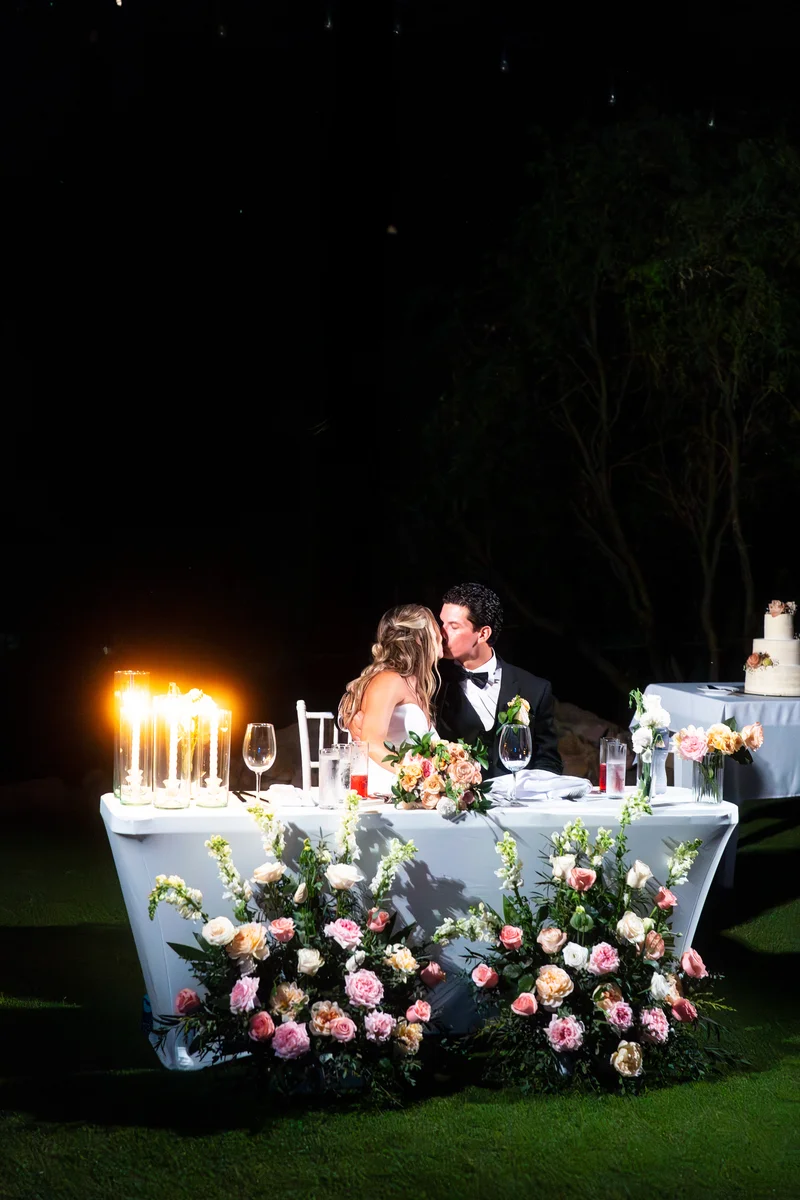 Los novios se besan en su mesa principal rodeada de rosas y velas por la noche