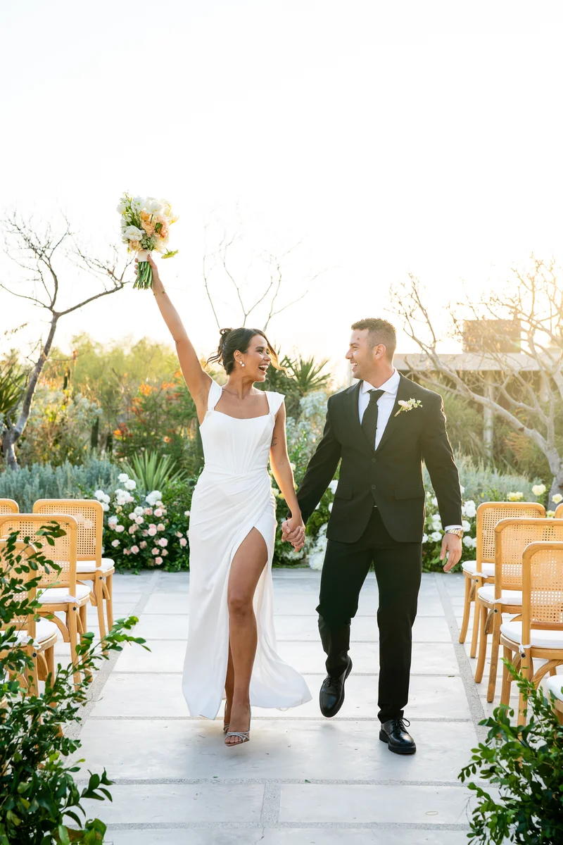 La novia levanta su ramo al salir de la ceremonia tomada de la mano del novio