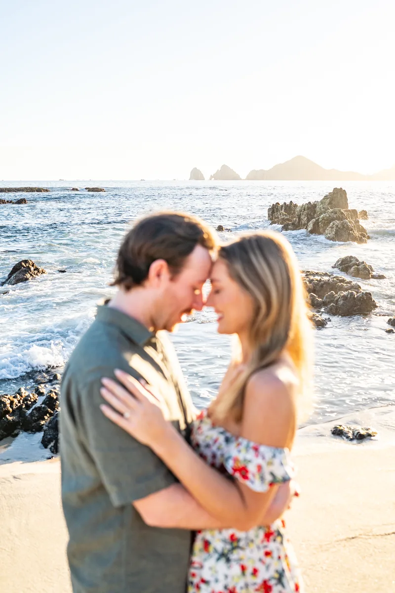 Pareja frente a frente en la playa al atardecer, con El Arco de Cabo San Lucas detrás